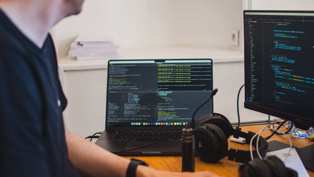 Personne travaillant sur un ordinateur avec des écrans montrant du code.
