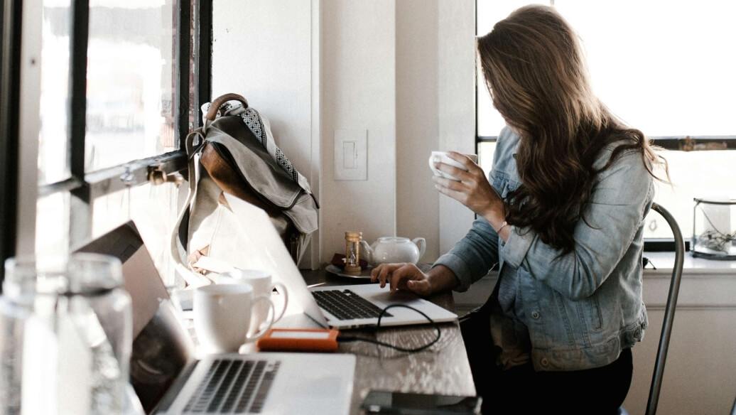 Personne à un bureau avec un ordinateur portable, buvant du café.