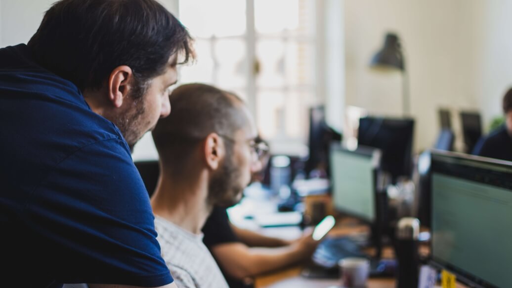 Deux hommes travaillent sur des ordinateurs dans un bureau lumineux.