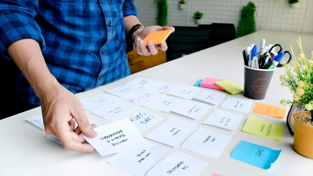 Personne organisant des cartes d'idées de contenus sur une table, avec des plantes et des fournitures de bureau.