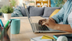 Personne tapant sur un ordinateur portable à une table avec des fournitures de bureau.