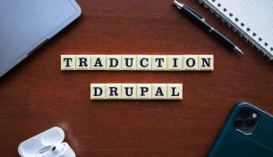 Lettres en bois formant "TRADUCTION DRUPAL" sur un bureau en bois, avec stylo et carnet. Image générée par l'IA