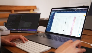 Deux ordinateurs portables sur un bureau en bois, affichant du code et un tableau.