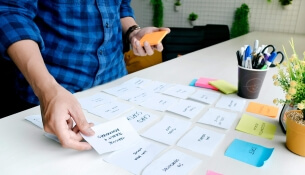 Personne organisant des cartes d'idées de contenus sur une table, avec des plantes et des fournitures de bureau.