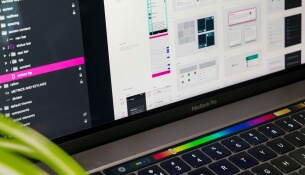 Ordinateur portable affichant des maquettes de design UI, plante verte au premier plan.