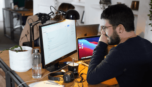 Homme travaillant devant des écrans d'ordinateur dans un bureau moderne.