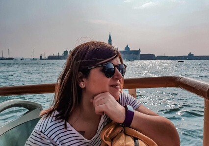 Marie, chef de projet Drupal chez Advency, portant des lunettes de soleil sur un bateau, avec Venise en arrière-plan.