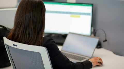 Personne travaillant sur un ordinateur portable, un écran avec une feuille de calcul en arrière-plan.